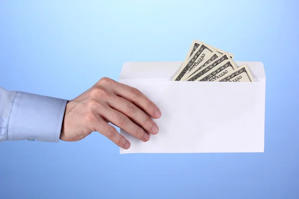 Man's hand holding an envelope with dollars on blue background — Stock Photo, Image