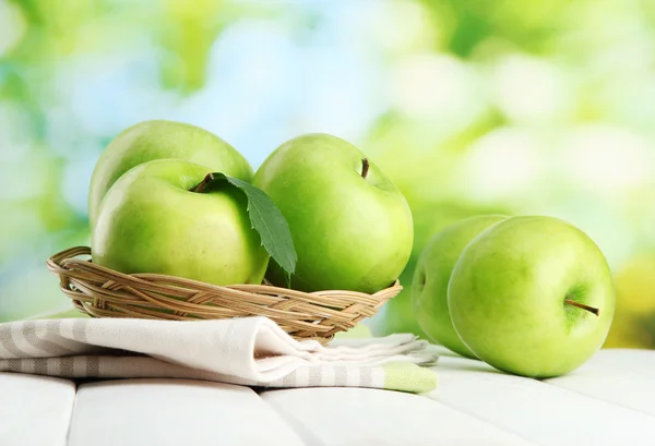 成熟的绿色苹果用叶子在篮子里，木桌上，在绿色背景上 — 图库照片
