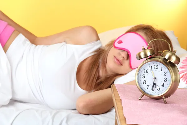 Jovem bela mulher dormindo na cama com máscara ocular e despertador — Fotografia de Stock