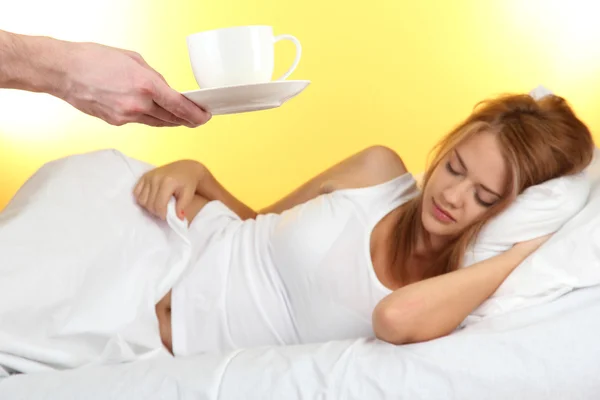 Morning coffee in bed for young woman on yellow background — Stock Photo, Image