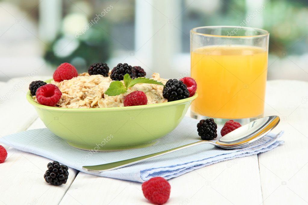 tasty oatmeal with berries and glass of juice on table, on window backgroun