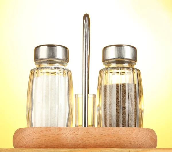 Salt and pepper mills, on wooden table on yellow background — Stock Photo, Image