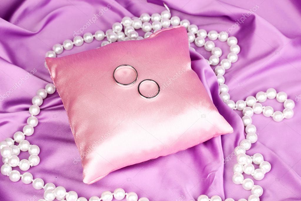 Wedding rings on satin pillow on purple cloth background Stock Photo by