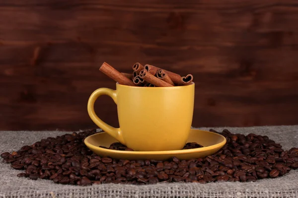 Zusammensetzung der gelben Tasse mit Kaffeebohnen und Zimt auf Holzboden — Stockfoto