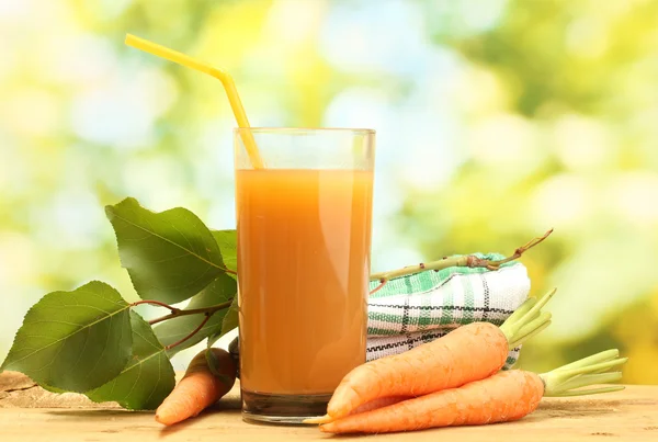 Glas morotsjuice och färska morötter på träbord på grön bakgrund — Stockfoto