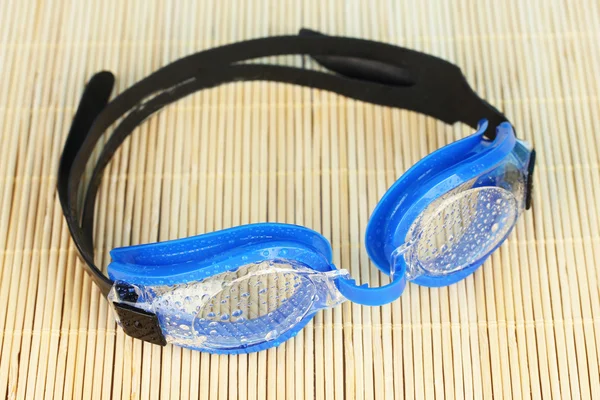 Blue swim goggles with drops on a bamboo pad — Stock Photo, Image