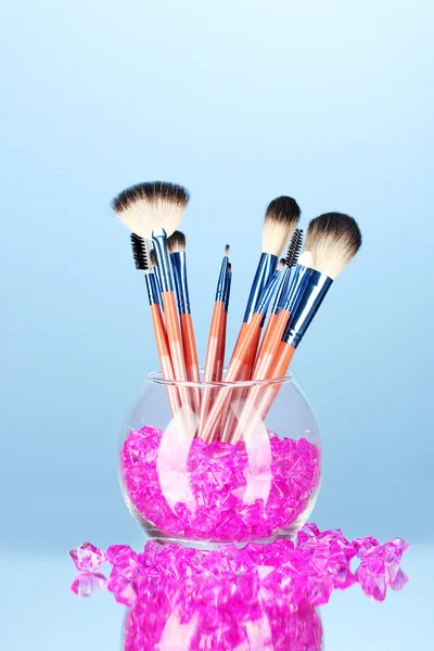 Make-up brushes in a bowl with stones on blue background — Stock Photo, Image