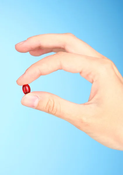 Ženská ruka držící červenou pilulku na modrém pozadí detail — Stock fotografie