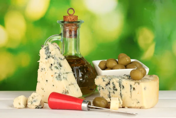 Samenstelling van blauwe kaas en olijven in een kom op groene achtergrond sluiten-u — Stockfoto