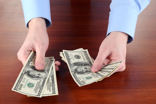 man recounts dollars on a wooden table close-up