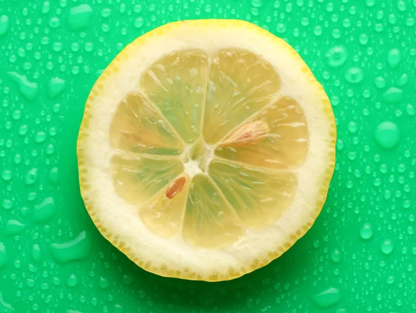Zitronenscheibe mit Tropfen auf grünem Hintergrund — Stockfoto