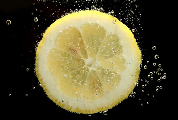 Rodaja de limón en el agua con burbujas, sobre fondo negro — Foto de Stock