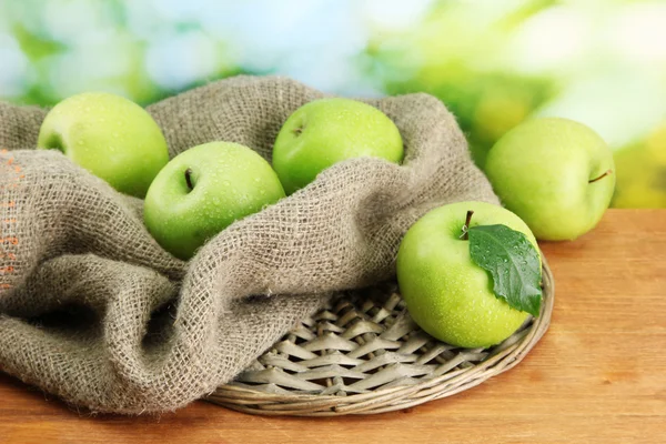 Ripe green apples with leaves on burlap, on wooden table, on green backgrou — Stock Photo, Image