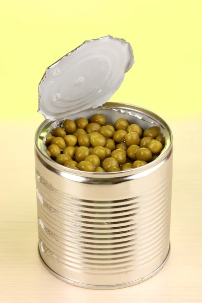 Open blikje van erwten op houten tafel op groene achtergrond — Stockfoto