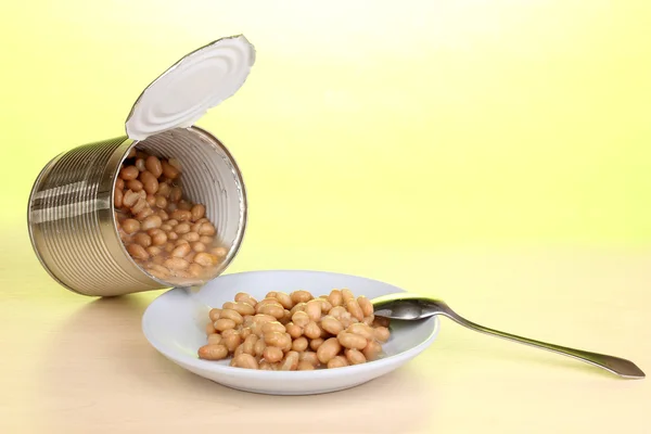 Open tin can and plate with bean and spoon on wooden table on green backgro — Stock Photo, Image