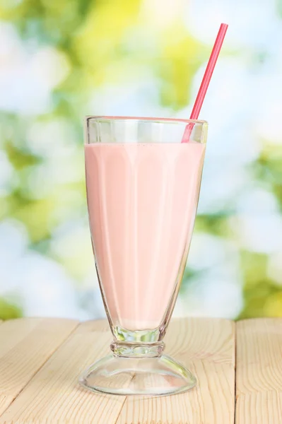 Batido de leite rosa na mesa de madeira no fundo brilhante — Fotografia de Stock