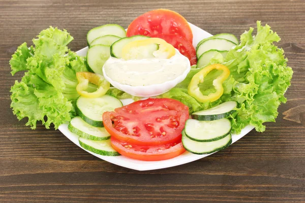 Chopped vegetables and sauce on plate on wooden table — Stock Photo, Image