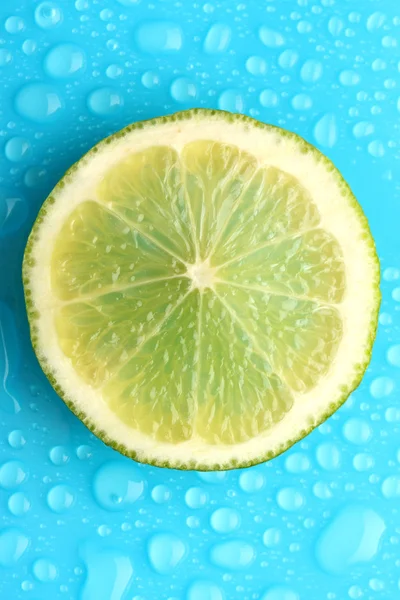 Tranche de citron vert avec goutte sur fond bleu — Photo