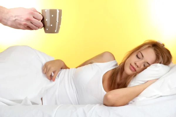 黄色の背景に若い女性のためのベッドでのコーヒーの朝 — ストック写真