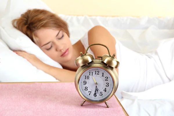 Young beautiful woman sleeping on bed with alarm clock in bedroom — Stock Photo, Image