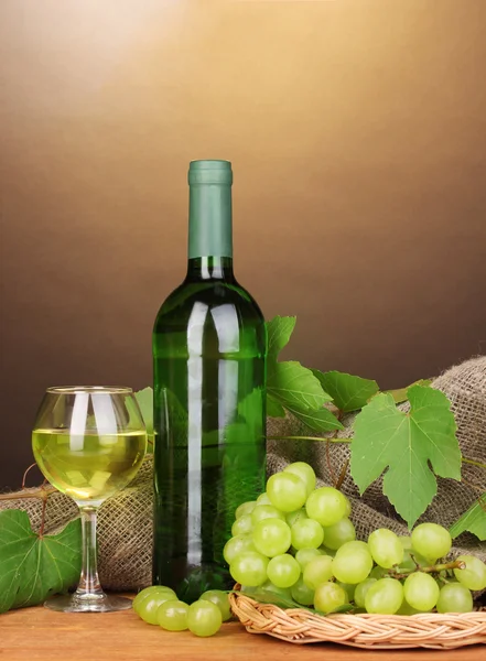 Láhev značkového vína se sklem na dřevěný stůl na hnědé pozadí — Stock fotografie