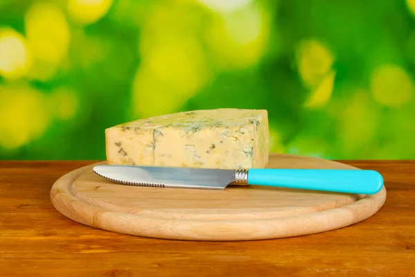 Cheese with mold and knife on the cutting board on bright green background — Stock Photo, Image