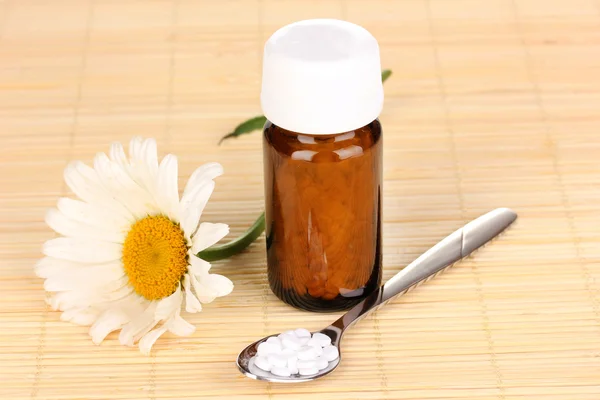 Flacone di medicinale con compresse e fiori su tappetino di bambù — Foto Stock