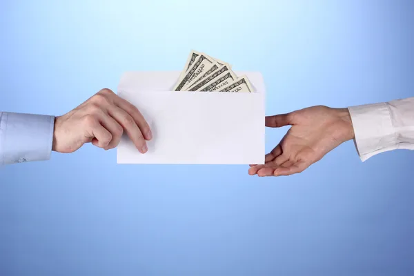 Mans hand passerar kuvertet med dollar på blå bakgrund — Stockfoto