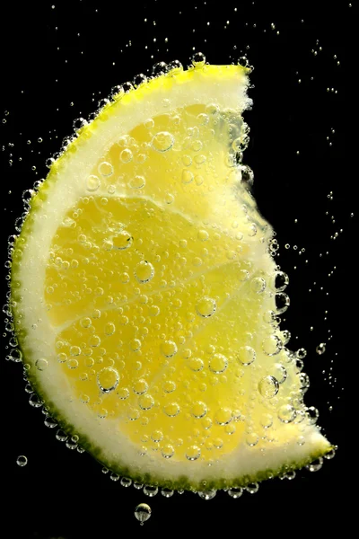 Fatia de limão na água com bolhas, sobre fundo preto — Fotografia de Stock