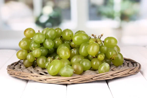 Uvas verdes maduras en cuna de mimbre sobre mesa de madera sobre fondo de ventana —  Fotos de Stock