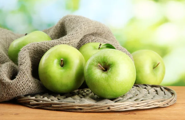 Manzanas verdes maduras en arpillera, sobre mesa de madera, sobre fondo verde — Foto de Stock
