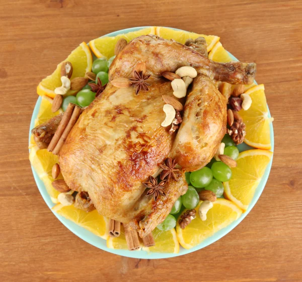 Geheel gebraden kip met druiven, sinaasappels en specerijen op blauw bord op hout — Stockfoto