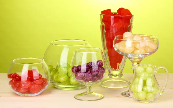 Color candies in glasses on wooden table on green background — Stock Photo, Image