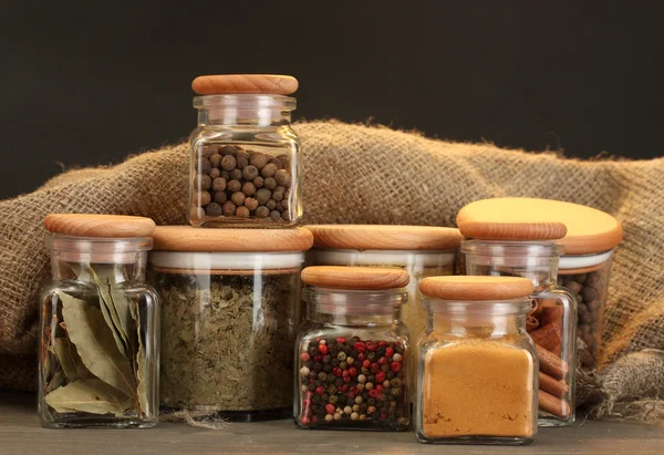 Jars with spices on wooden table on black background — Stock Photo, Image