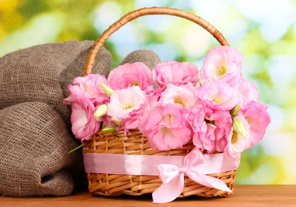 Bouquet of eustoma flowers in basket, on wooden table, on green background — Stock Photo, Image