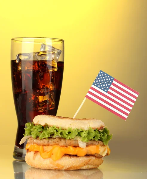 Tasty sandwich with american flag and cola, on yellow background — Stock Photo, Image