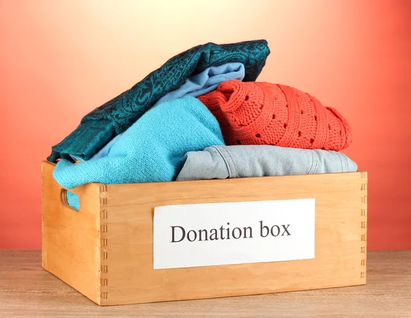 Donatie box met kleding op rode achtergrond close-up — Stockfoto