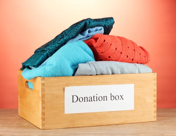 Donation box with clothing on red background close-up — Stock Photo, Image