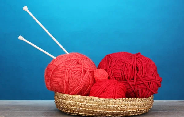 Red knittings yarns in basketon on wooden table on blue background — Stock Photo, Image