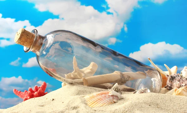 Glass bottle with note inside on sand, on blue sky background — Stock Photo, Image