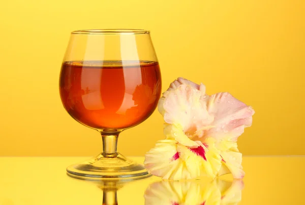 Glass with cocktail and gladiolus bud on yellow background close-up — Stock Photo, Image