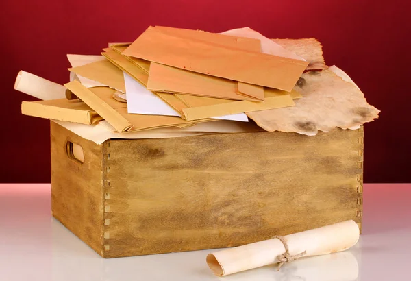 Caixa de madeira com papéis e letras sobre fundo vermelho — Fotografia de Stock