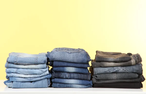 Många jeans staplade i en högar på gul bakgrund — Stockfoto