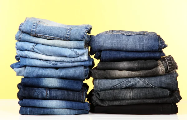 Många jeans staplade i en högar på gul bakgrund — Stockfoto