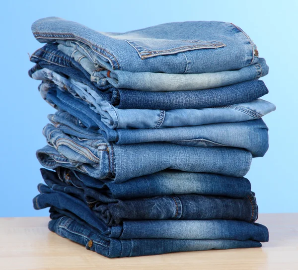 Många jeans staplade i en hög på blå bakgrund — Stockfoto