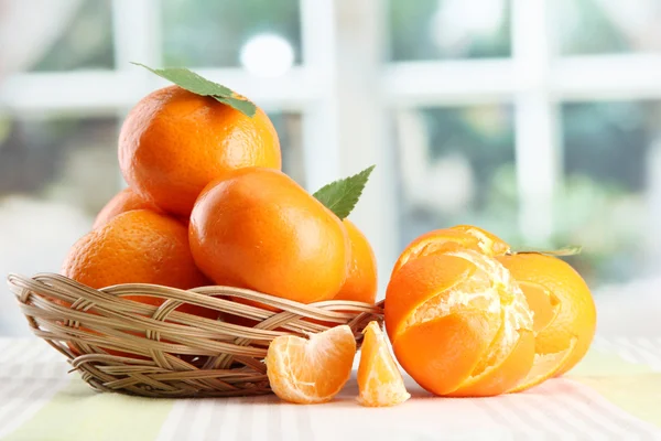 Tangerines with leaves in a beautiful basket, on table on window background — Stock Photo, Image