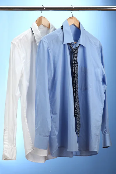 Cămăși albastre și albe cu cravată pe cuier de lemn pe fundal albastru — Fotografie, imagine de stoc