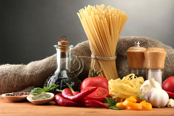 Pasta spagetti, grönsaker och kryddor, på träbord, på grå bakgrund — Stockfoto