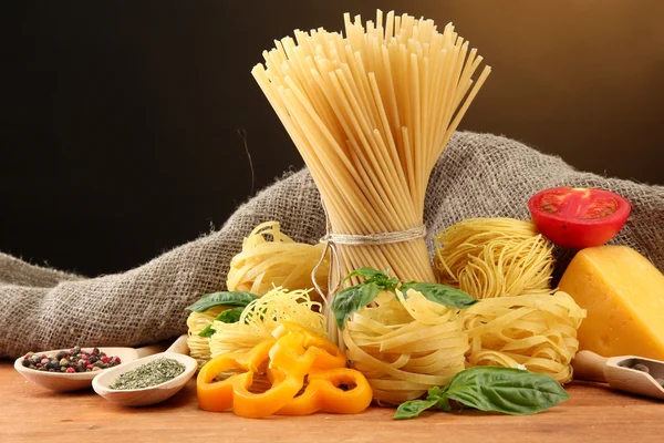 Nudelspaghetti, Gemüse und Gewürze, auf Holztisch, auf braunem Hintergrund — Stockfoto