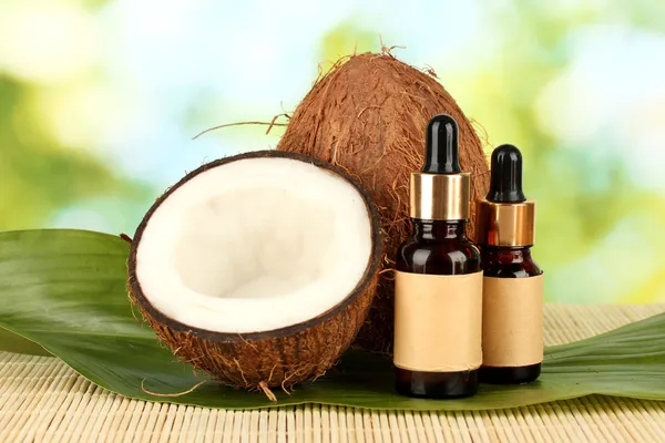 Kokosový olej v lahví s kokosy na zeleném pozadí — Stock fotografie